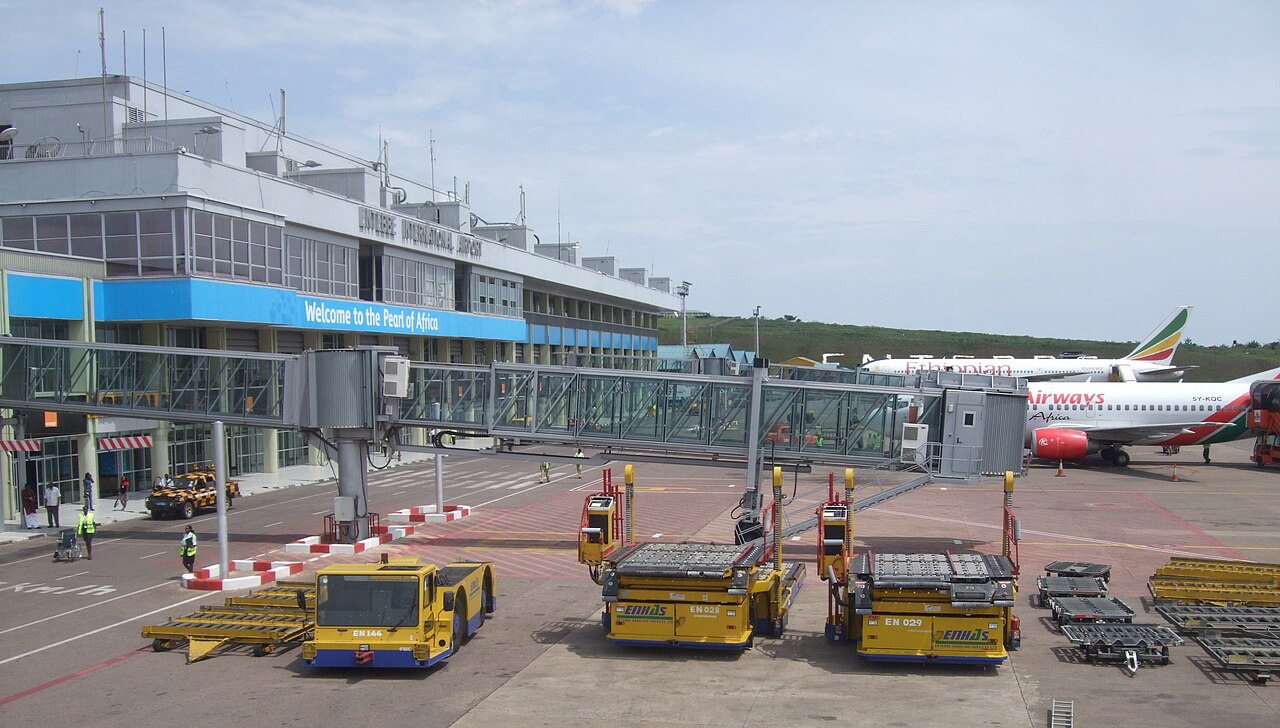 Entebbe International Airport terminal with boarding bridges, parked aircraft and yellow ground vehicles.
