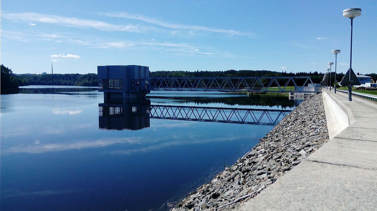 Still water at Římov Reservoir, with an intake tower and walkway beside the dam.