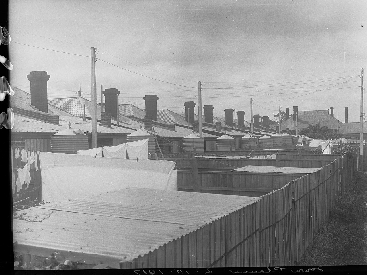 Historic black-and-white view of corrugated rainwater tanks behind a row of Adelaide houses