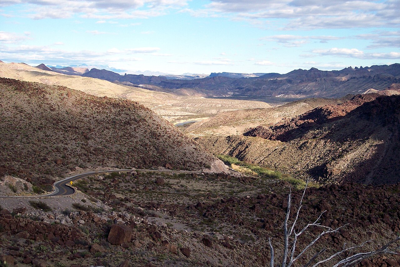 A paved road winds through rocky desert hills, with the Rio Grande and distant mountains in Big Bend National Park.