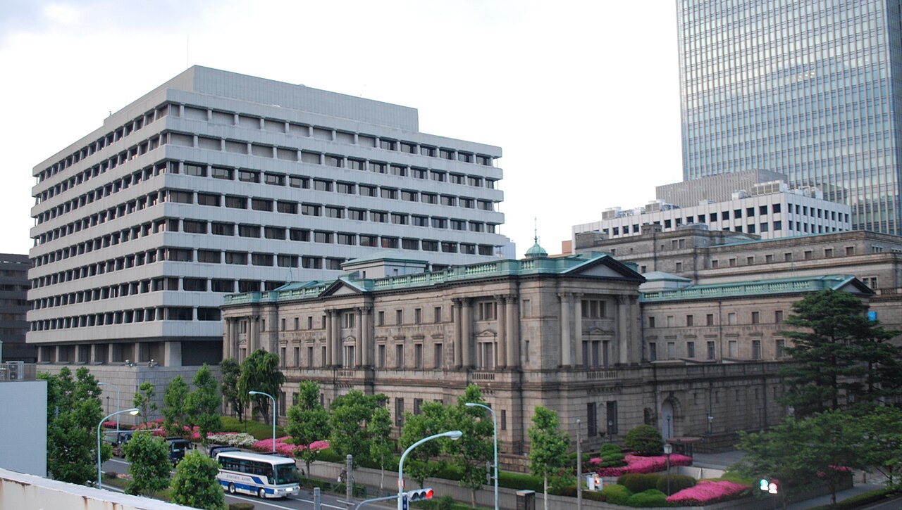 The Bank of Japan’s stone head office with a green roof, surrounded by taller buildings in Tokyo.