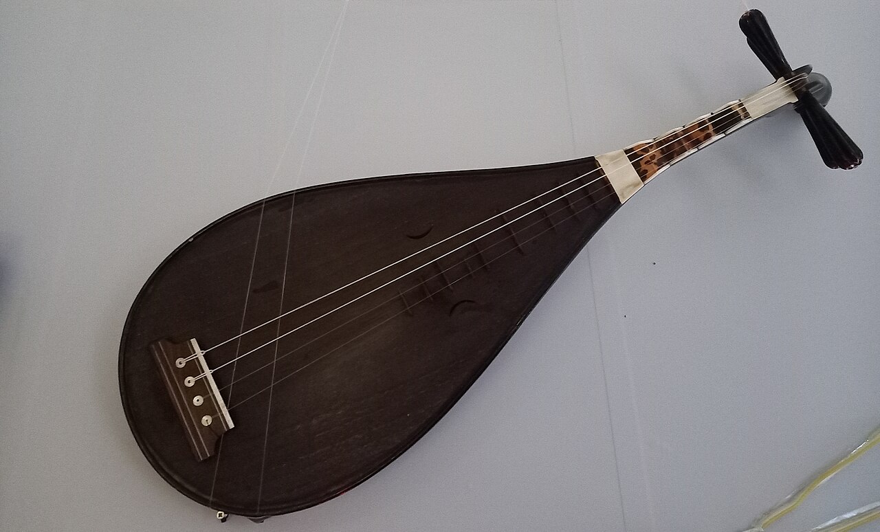 Dark wooden nanguan pipa with four strings and a crooked neck, displayed against a pale background.