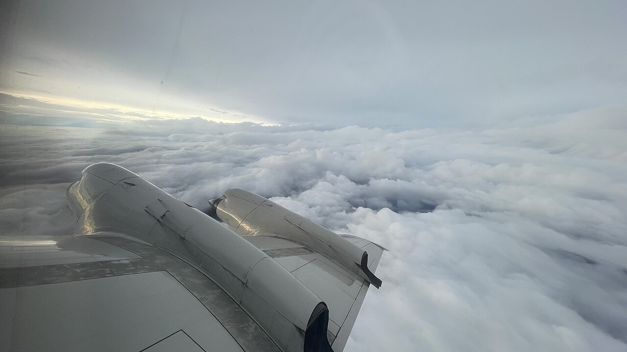 View over the wing of a NOAA WP-3D Orion aircraft flying above dense tropical-storm clouds.