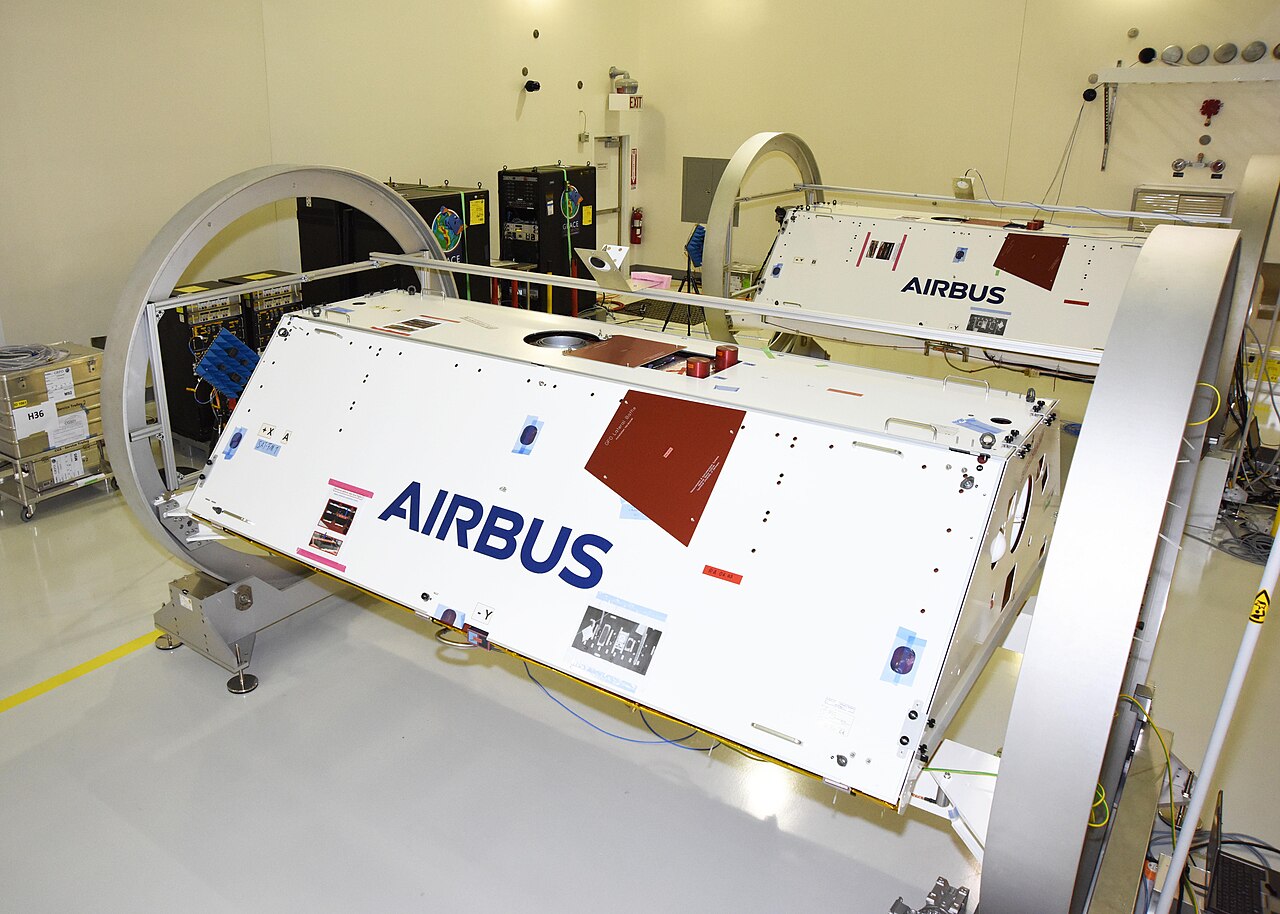 Two white GRACE Follow-On satellites mounted on circular turntable fixtures inside a clean room.