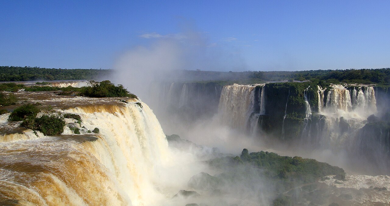 Broad cascades at Iguazú Falls plunge past forested islands into a mist-filled gorge.