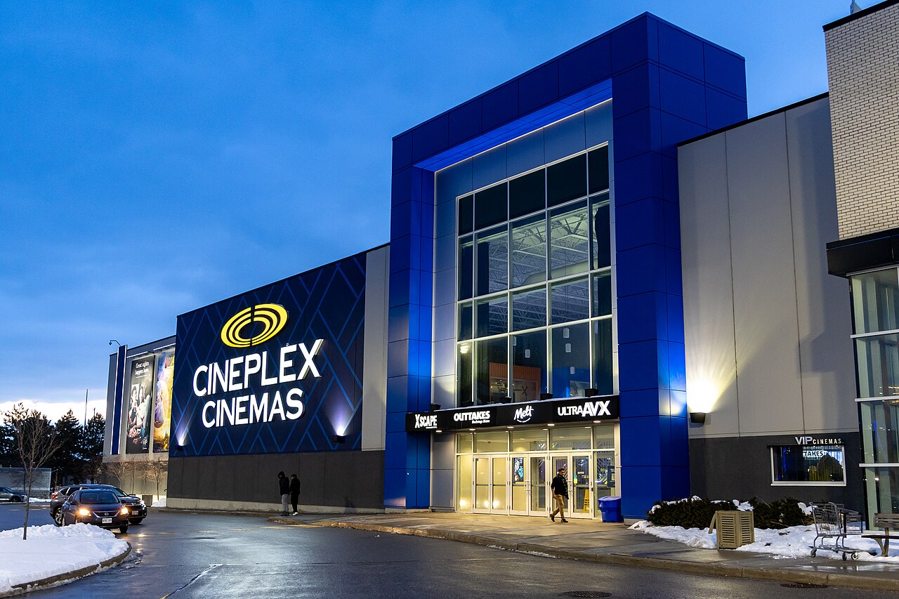 Snow surrounds the illuminated entrance of a Cineplex Cinemas theater in Pickering, Ontario, at dusk.