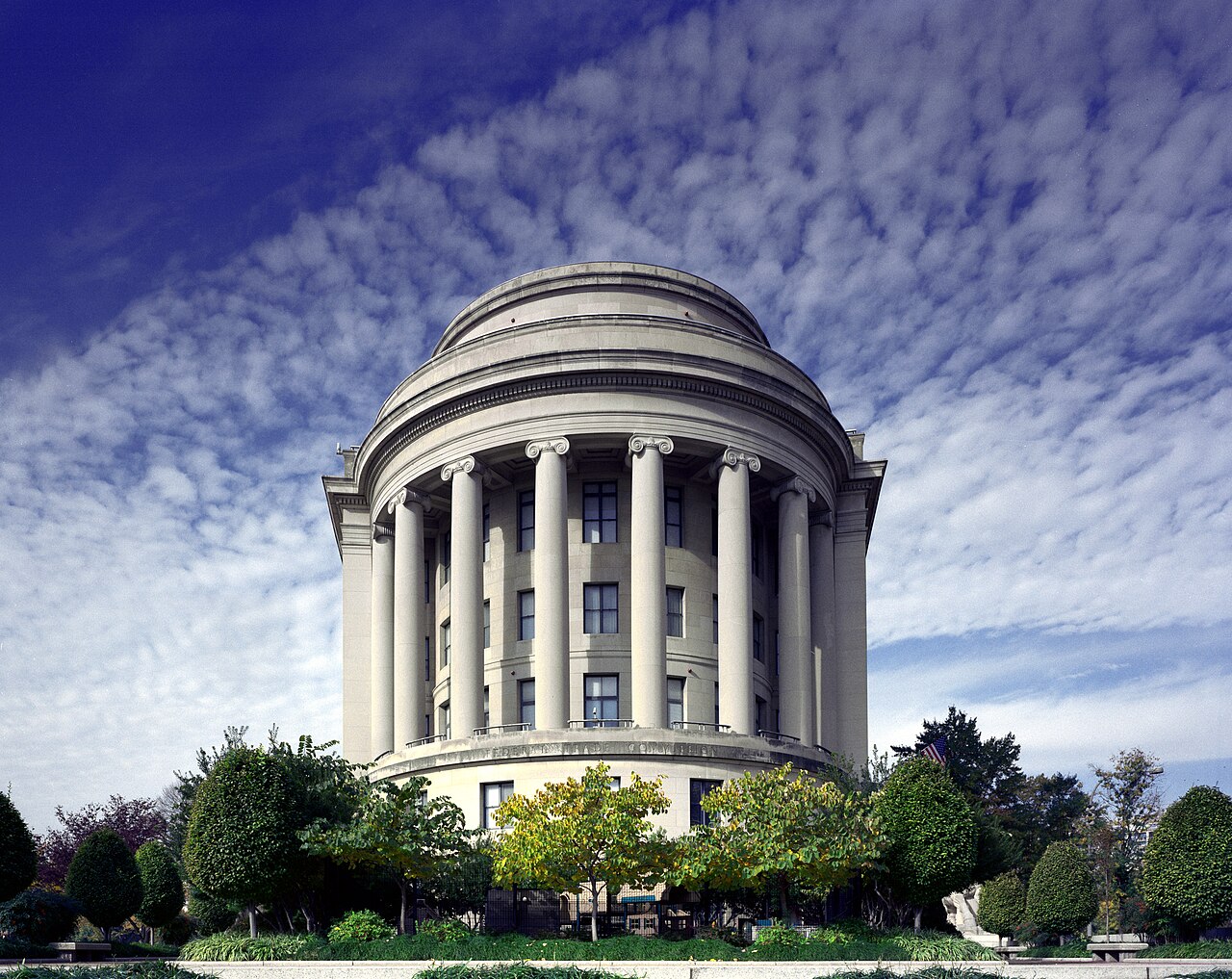 Rounded stone facade and tall columns of the Federal Trade Commission building, framed by trees.